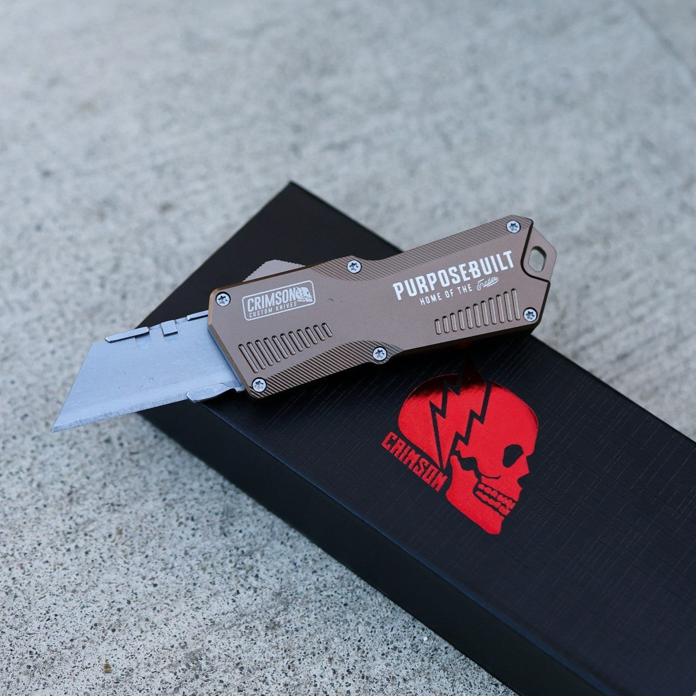 Folding knife on a black surface with a red logo, on a gray concrete background