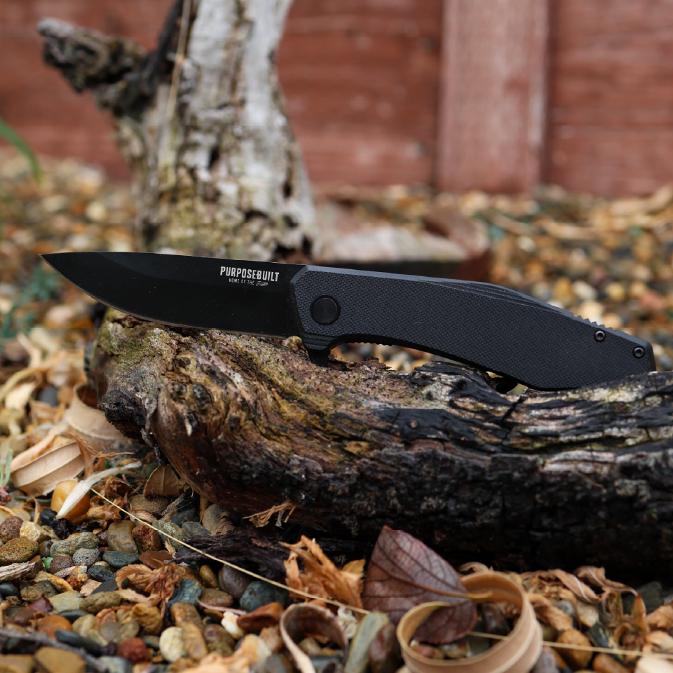 Crimson × Purpose-Built M6 Folder resting on a log outdoors