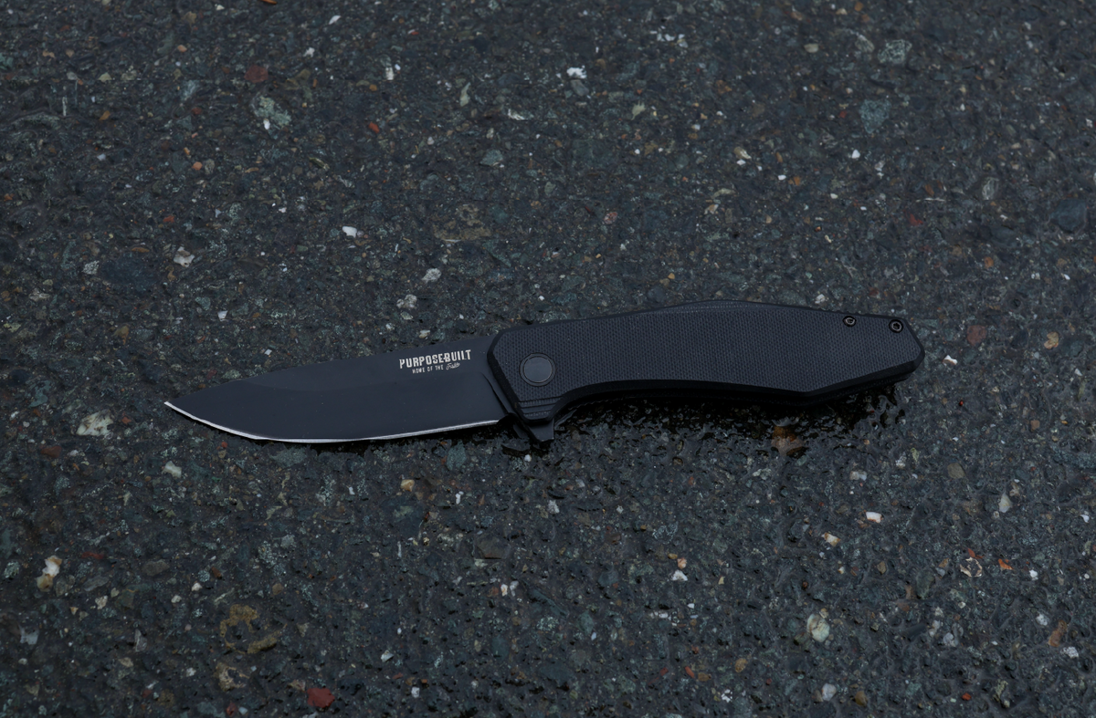 Crimson × Purpose-Built M6 Folder knife, black on black, on wet asphalt