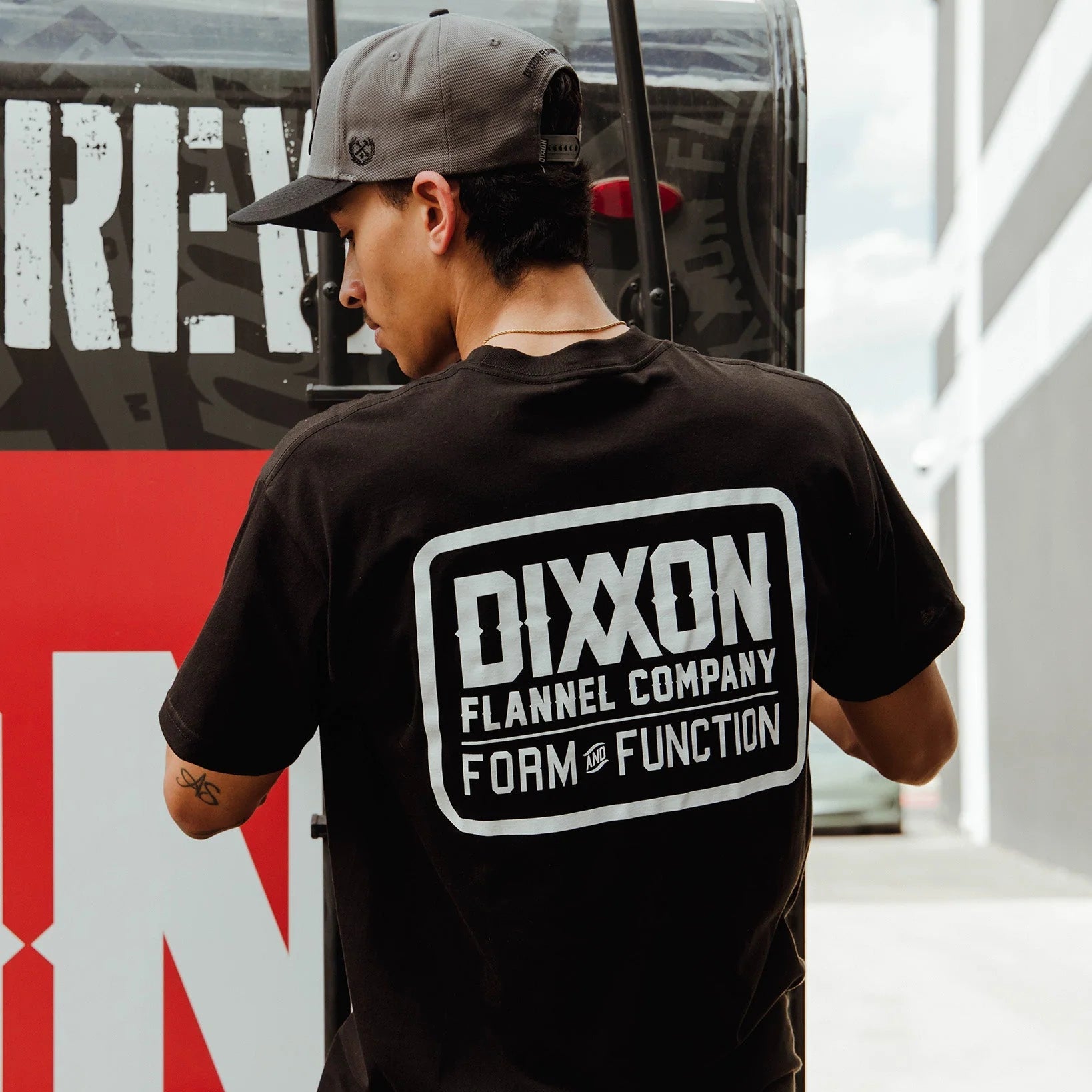 Person wearing a black t-shirt with 'Dixxon Flannel Company' logo, standing in front of a red and white background.