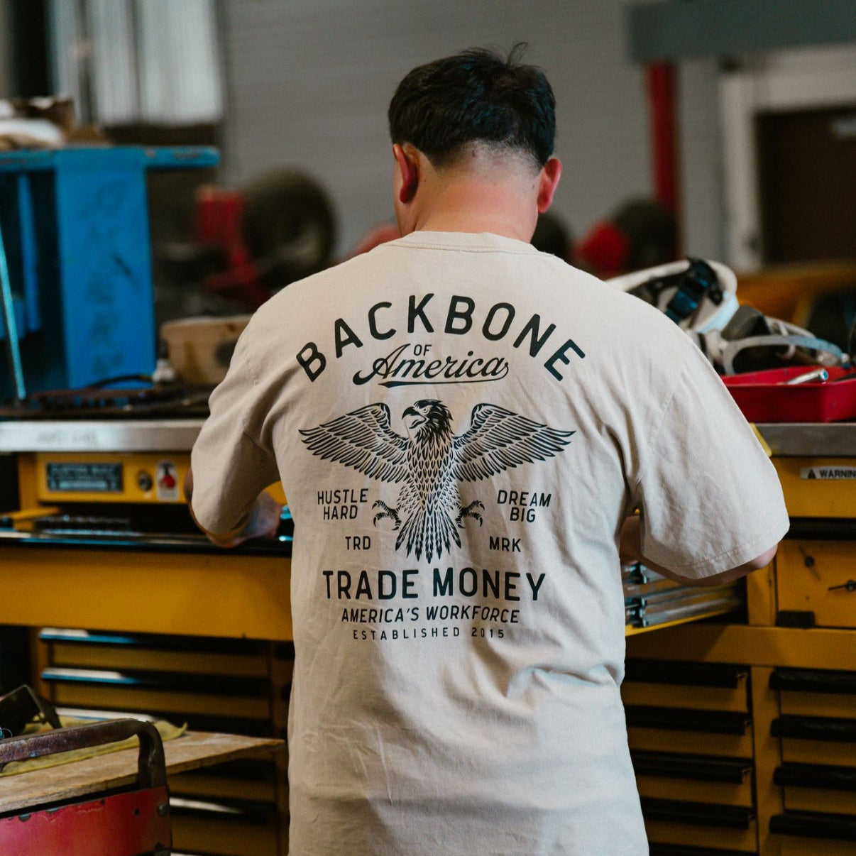 Person wearing a t-shirt with 'Backbone America' design in a workshop setting