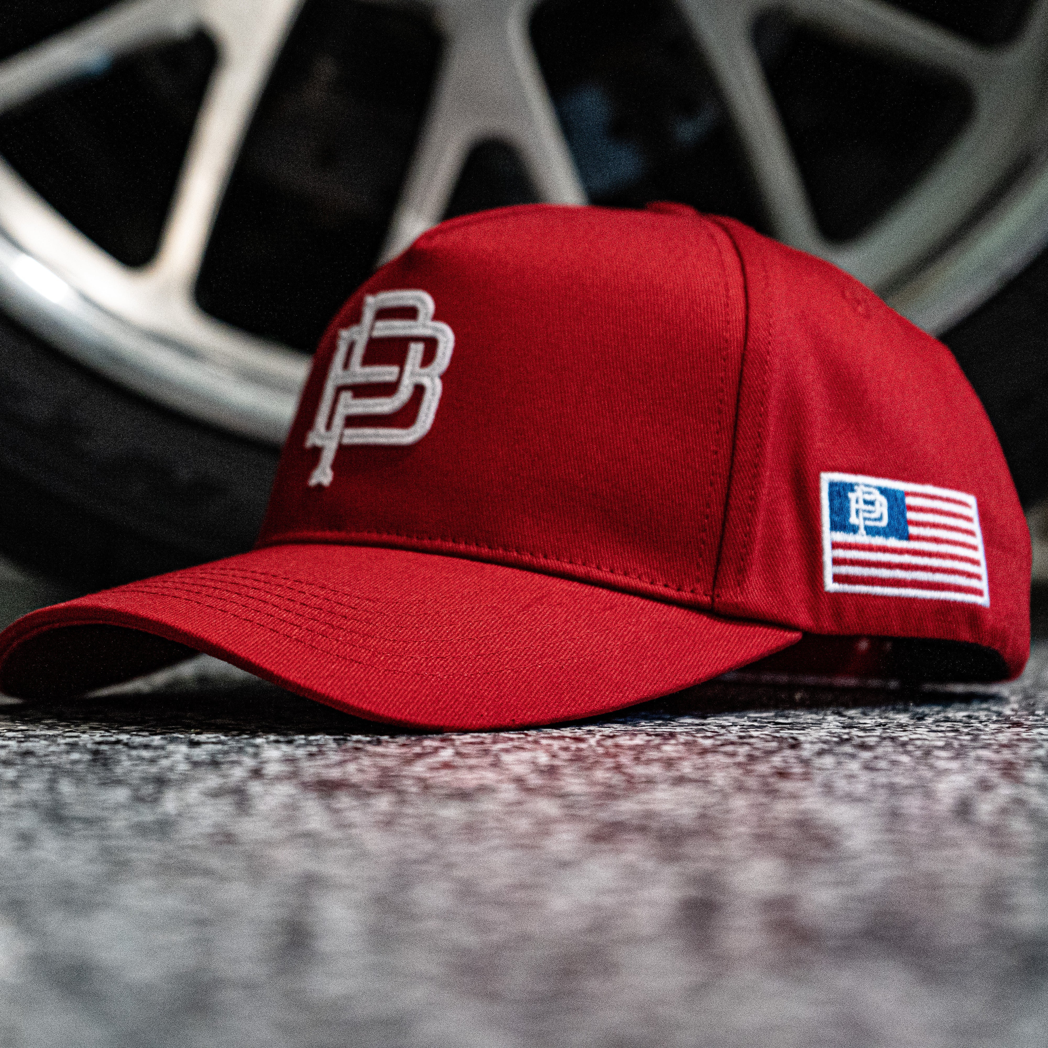 Red cap with a logo and American flag patch on a textured surface with a blurred wheel in the background